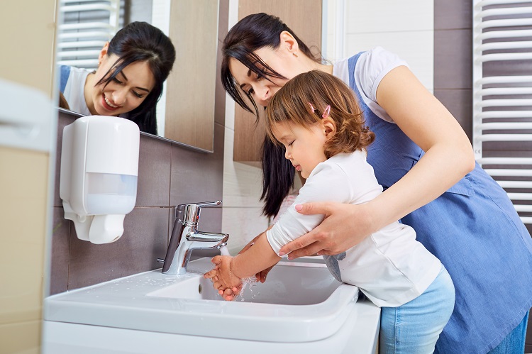 Kid washing hands with mom in the bathroom.