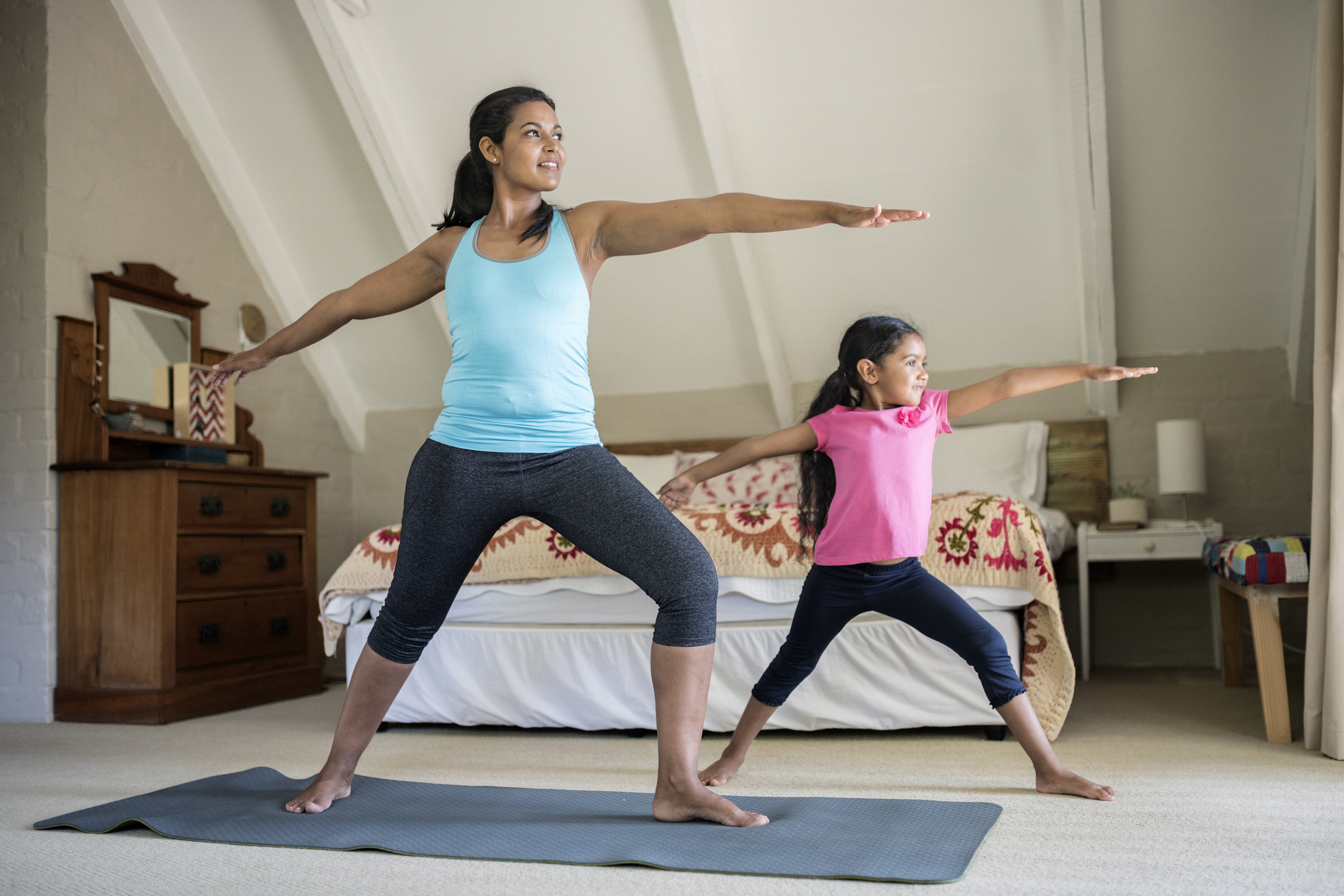 Mother and daughter practicing yoga. Females are exercising in bedroom. They are at home.